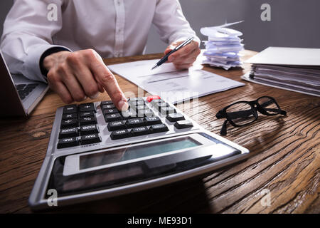 Der Unternehmer Hand Berechnung Bill mit Taschenrechner auf hölzernen Schreibtisch Stockfoto