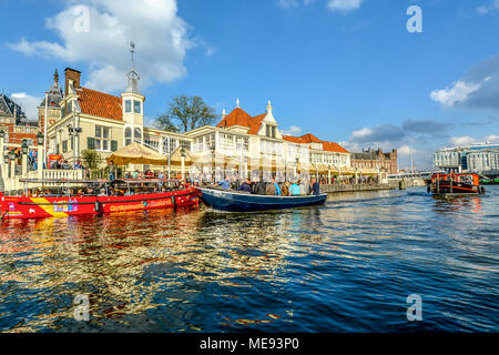 Touristen Menge eine Tour Boot vor ein open Air Cafe neben dem Kanal mit dem zentralen Bahnhof hinter Stockfoto