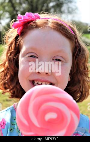 Eine rothaarige Behaarte Mädchen in ein schickes blaues Kleid mit einem großen, rosa und weißen Lollipop Stockfoto