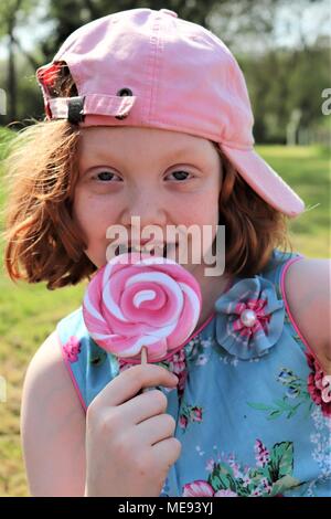 Eine rothaarige Behaarte Mädchen in ein schickes blaues Kleid mit einem großen, rosa und weißen Lollipop Stockfoto