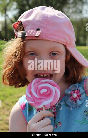 Eine rothaarige Behaarte Mädchen in ein schickes blaues Kleid mit einem großen, rosa und weißen Lollipop Stockfoto