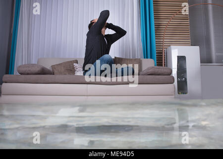 Mann auf Sofa mit Hände auf den Kopf Umkippen in Zimmer überflutet mit Wasser Stockfoto