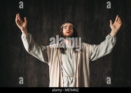 Jesus Christus in ein weißes Gewand betet emotional mit seinen Händen, dunklen Hintergrund. Sohn Gottes, einen starken Glauben an Gott Stockfoto