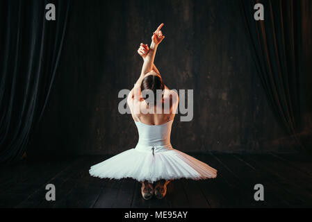 Weibliche klassisches Ballett Performer in weißem Kleid auf dem Boden sitzend, Ansicht von hinten. Ballerina Training in der Klasse mit Fenster Stockfoto