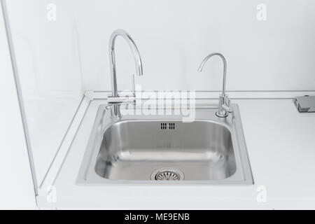 Metall chrom Waschbecken mit zwei Hähnen, schlicht und gefiltertes Wasser. Fragment der modernen Küche mit Theke und einem Waschbecken. Detail des Inneren Stockfoto
