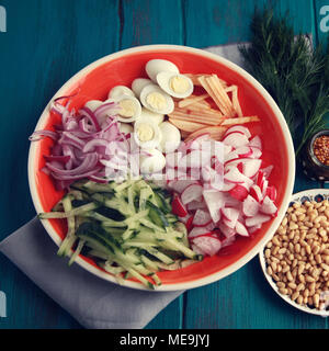 Zutaten für eine Wachtel eier Salat auf die runde Platte. Europäische Küche. Eier, Radieschen, Gurke in Scheiben geschnitten und Pinienkernen. Bunte Foto. Blau Holz- ba Stockfoto