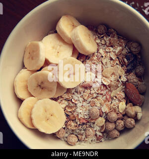 Müsli Schale mit Banane, Rosinen und Nüssen und auf dem Holz- Hintergrund. Nahaufnahme Foto. Gesundes Frühstück. Ansicht von oben. Sweet vegane Gerichte. Morgen oatmea Stockfoto
