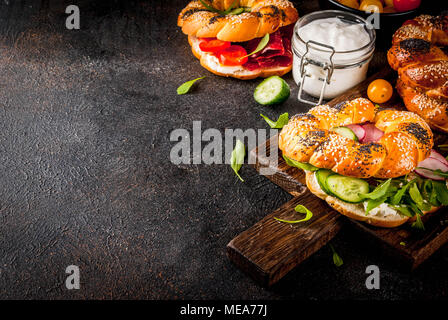 Auswahl an hausgemachten Bagels Sandwiches mit Sesam und Mohn, Frischkäse, Schinken, Radieschen, Rucola, Tomaten, Gurken, mit Zutaten o Stockfoto