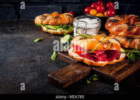 Auswahl an hausgemachten Bagels Sandwiches mit Sesam und Mohn, Frischkäse, Schinken, Radieschen, Rucola, Tomaten, Gurken, mit Zutaten o Stockfoto