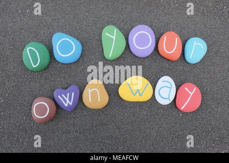 Ihre eigene Art und Weise, Sms mit bunten Steinen über schwarzen vulkanischen Sand Stockfoto