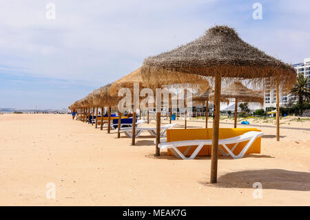 Reihen von Stroh, Liegestühlen und Sonnenschirme am Strand von Vilamoura, Algarve, Portugal. Stockfoto