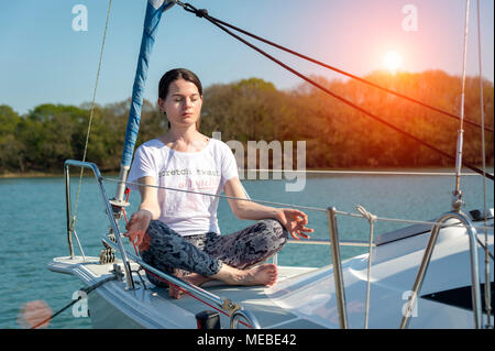 Frau sitzt auf dem Deck einer Segelyacht im Lotussitz, Yoga Stockfoto