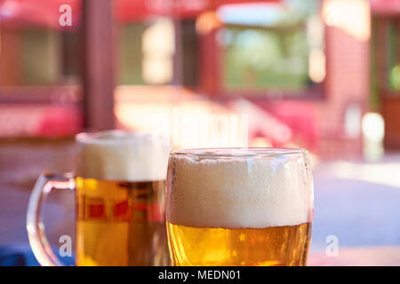 Zwei Gläser Bier auf dem Tisch zu stehen in einem Garten Pub auf ein Sommer sonnigen Tag mit einem unscharfen Hintergrund Stockfoto