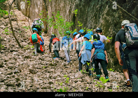 Tscherven bryag, Bulgarien, 15. April 2018: hintere Ansicht aus einer Reihe von Kindern im Alter von 7-10 das Tragen von Schutzhelmen und Leitung von Bergführern Wanderung zwischen den Felsen Stockfoto