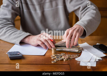 Close up Mann mit Taschenrechner zählen, Notizen zu Hause, in der Hand ist, schreibt in einem Notebook. Gestapelte Münzen angeordnet an deesk. Einsparungen Finanzen Konzept. Stockfoto