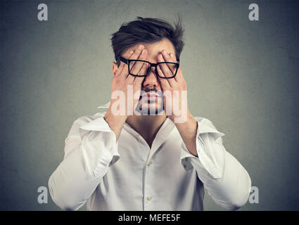 Closeup Portrait junger Mann in Gläser für Gesicht Augen mit beiden Händen auf grauen Hintergrund isoliert Stockfoto