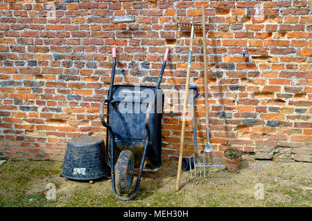 Traditionelle Gartengeräte schubkarre zwei Rechen und Gabel ein Kunststoff flexi Whirlpool von einer alten Mauer in Helmsley Walled Garden North Yorkshire Stockfoto