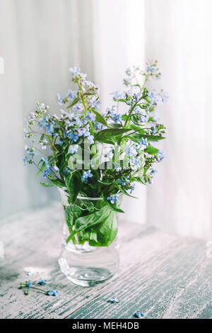 Blumenstrauß aus Vergissmeinnicht in einem durchsichtigen Glas Vase. Auf hölzernen Tisch am Fenster Hintergrund. Stockfoto