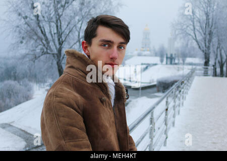 Junge schöne europäische Kerl in warmen Mantel und Schal auf der snow-covered Bridge während der kalten Winter Stockfoto