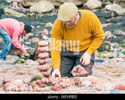 Dunbar, Schottland, 22. April 2018. Auge Cave Strand, Dunbar, East Lothian, Schottland, Vereinigtes Königreich. In der zweiten Europäischen Stein stacking Meisterschaft, von Dunbar Street Art Trail organisiert. Die abschließende Konkurrenz war die meisten künstlerischen Stein Balance zu schaffen. James Brunt, einem Wettbewerber aus England, erstellt einen Stein ausgewogenes Kunstwerk auf den Strand, einen Vergnügungspark mit Achterbahn Stockfoto