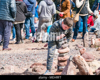 Dunbar, Schottland, 22. April 2018. Auge Cave Strand, Dunbar, East Lothian, Schottland, Vereinigtes Königreich. In der zweiten Europäischen Stein stacking Meisterschaft, von Dunbar Street Art Trail organisiert. Die abschließende Konkurrenz war die meisten künstlerischen Stein Balance zu schaffen. Ein Junge versucht seine Hand am Stein Balancieren auf den Strand Stockfoto