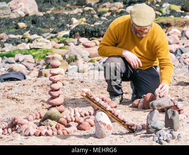 Dunbar, Schottland, 22. April 2018. Auge Cave Strand, Dunbar, East Lothian, Schottland, Vereinigtes Königreich. In der zweiten Europäischen Stein stacking Meisterschaft, von Dunbar Street Art Trail organisiert. Die abschließende Konkurrenz war die meisten künstlerischen Stein Balance zu schaffen. James Brunt, einem Wettbewerber aus England, erstellt einen Stein ausgewogenes Kunstwerk auf den Strand, einen Vergnügungspark mit Achterbahn Stockfoto