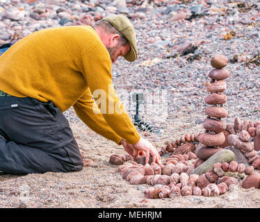 Dunbar, Schottland, 22. April 2018. Auge Cave Strand, Dunbar, East Lothian, Schottland, Vereinigtes Königreich. In der zweiten Europäischen Stein stacking Meisterschaft, von Dunbar Street Art Trail organisiert. Die abschließende Konkurrenz war die meisten künstlerischen Stein Balance zu schaffen. James Brunt, einem Wettbewerber aus England, erstellt einen Stein ausgewogenes Kunstwerk auf den Strand, einen Vergnügungspark mit Achterbahn Stockfoto