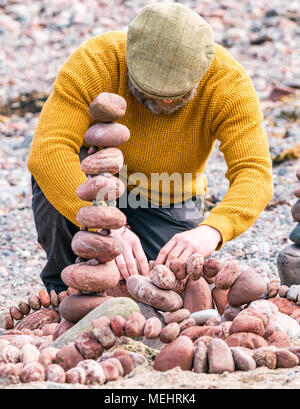 Dunbar, Schottland, 22. April 2018. Auge Cave Strand, Dunbar, East Lothian, Schottland, Vereinigtes Königreich. In der zweiten Europäischen Stein stacking Meisterschaft, von Dunbar Street Art Trail organisiert. Die abschließende Konkurrenz war die meisten künstlerischen Stein Balance zu schaffen. James Brunt, einem Wettbewerber aus England, erstellt einen Stein ausgewogenes Kunstwerk auf den Strand, einen Vergnügungspark mit Achterbahn Stockfoto