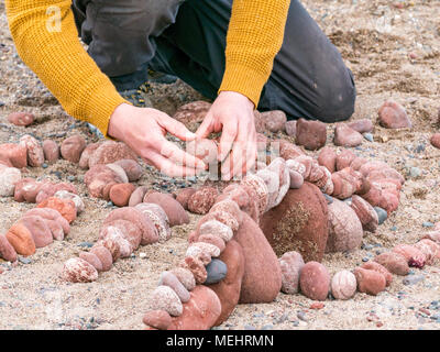 Dunbar, Schottland, 22. April 2018. Auge Cave Strand, Dunbar, East Lothian, Schottland, Vereinigtes Königreich. In der zweiten Europäischen Stein stacking Meisterschaft, von Dunbar Street Art Trail organisiert. Die abschließende Konkurrenz war die meisten künstlerischen Stein Balance zu schaffen. James Brunt, einem Wettbewerber aus England, erstellt einen Stein ausgewogenes Kunstwerk auf den Strand, einen Vergnügungspark mit Achterbahn Stockfoto