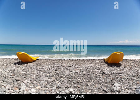 Zwei gelben Kunststoff liegen am Strand mit Blick auf das Mittelmeer Wellen an einem sonnigen Tag Stockfoto