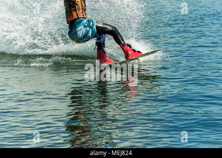 Wakeboarder springt von einem Sprungbrett hinter einem Seil und macht eine Welle auf dem Wasser. Stockfoto