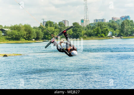 Wakeboarder springt von einem Sprungbrett hinter einem Seil und macht eine Welle auf dem Wasser. Stockfoto