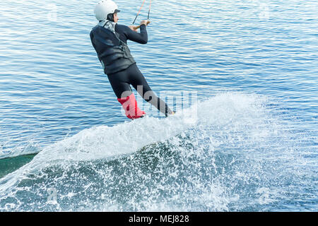 Wakeboarder springt von einem Sprungbrett hinter einem Seil und macht eine Welle auf dem Wasser. Stockfoto