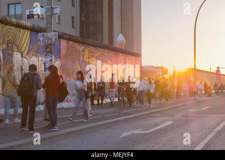 Berlin, Deutschland - April 2018: Junge Menschen zu Fuß an der Berliner Mauer (East Side Gallery) auf Sommer Tag abends bei Sonnenuntergang Himmel Stockfoto