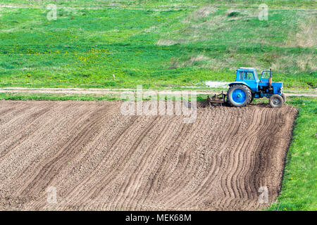 Blue dusty Traktor mit saatbeet Kultivator stehen am Rande des frisch gepflügt und bebautes Feld, den Boden für die Aussaat vorbereitet. Landwirtschaft, Landwirtschaftliche Stockfoto