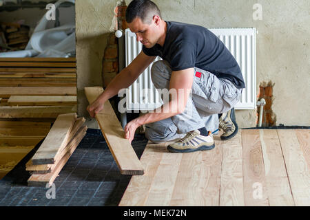 Junge schöne professionelle Tischler Installation von natürlichen hölzernen Planken auf Holzrahmen, in leeren unfertiges Zimmer unter Rekonstruktion. Improvemen Stockfoto