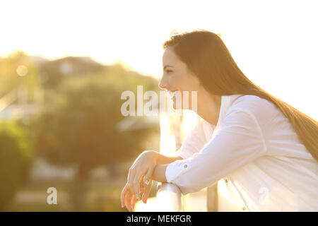 Seitenansicht Portrait Of Happy brunette Frau weg in einen Balkon bei Sonnenuntergang Stockfoto