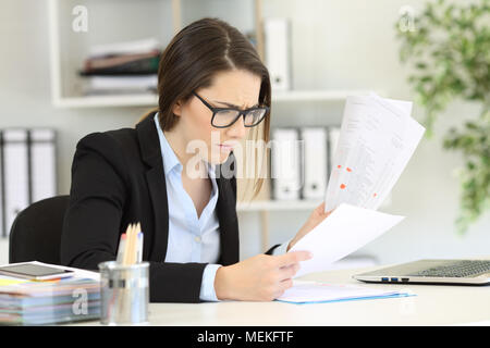 Besorgt Büroangestellter lesen Sales Reports in einem Desktop sitzen am Arbeitsplatz Stockfoto