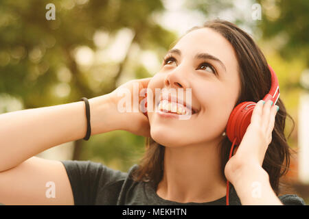 Portrait von junge schöne Frau mit roten Kopfhörer Musik hören. Im Freien. Städtebauliche Konzept. Stockfoto