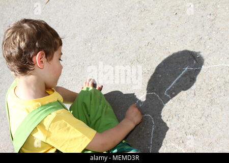 Cute Boy mit farbigen Kreiden auf einem Kinderspielplatz schreiben. Kleines Kind zieht mit Kreiden. Ferienhäuser Konzept. Bildung Konzept. Schule und lustige Zeit. Spielen Stockfoto