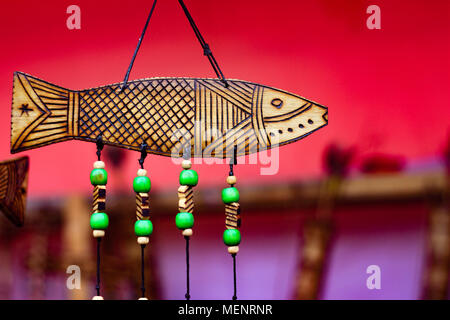 Hand aus Holz schnitzen graviert Fisch Abbildung Kunstwerke auf Holz Plank mit gefederter grüne Perlen auf String. tribal Artwork. strukturierten Hintergrund Stockfoto