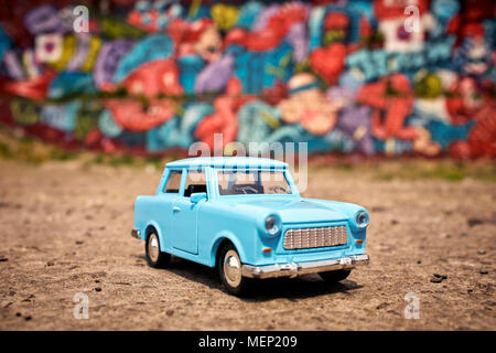 Eine blaue Spielzeug Trabant vor einer Wand mit Graffiti in Berlin Deutschland EU-lackiert. Stockfoto