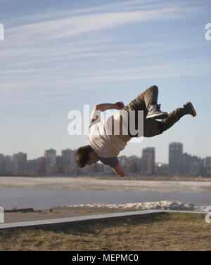 Junger Mann parkour Sportler führt Tricks vor der Skyline Stockfoto