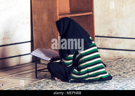 Eine muslimische Frau mit einem schwarzen Kopftuch sitzt vor dem Koran in einer Moschee und liest ein Gebet aus dem Koran. Gebete während des heiligen Monats Ramad Stockfoto