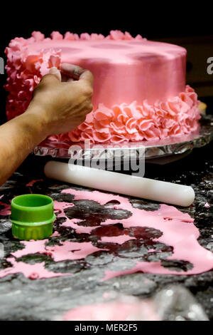 Verziert eine Torte rosa Zuckerglasur Blütenblätter werden auf Home sind rosa Zuckerglasur Kuchen von asiatischen weiblichen Hand vor den Kuchen und ist ein weisses roliin Stockfoto