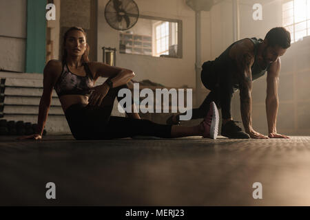 Fitness-Leute, die Dehnungsübungen im Fitnessstudio machen. Junge Frau, die sich mit Fitnesstrainer im Fitnessstudio aufhält. Stockfoto