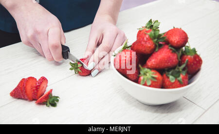 Eine Nahaufnahme Bild eines Mädchen Hände halten ein Messer und Vorbereitung von Obst durch Messern von Erdbeeren in Ihrer Küche Stockfoto