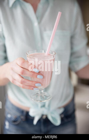 Im mittleren Abschnitt eine modische Mädchen mit Pastellfarben und halten ein volles Glas der Erdbeere Smoothie oder Milchshake mit einem rosa Stroh Stockfoto