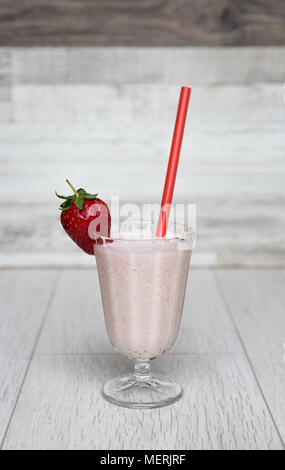 Ein Pastell rosa Erdbeer Milchshake oder Smoothie in einem hohen Glas mit frischem Obst und einem roten Stroh auf einem weißen Hintergrund eingerichtet. Stockfoto