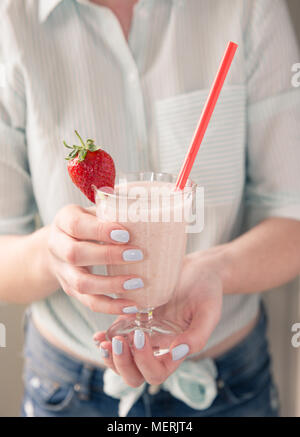 Im mittleren Abschnitt eine modische Mädchen mit Pastellfarben und halten ein volles Glas der Erdbeere Smoothie oder Milchshake mit einem rosa Stroh Stockfoto